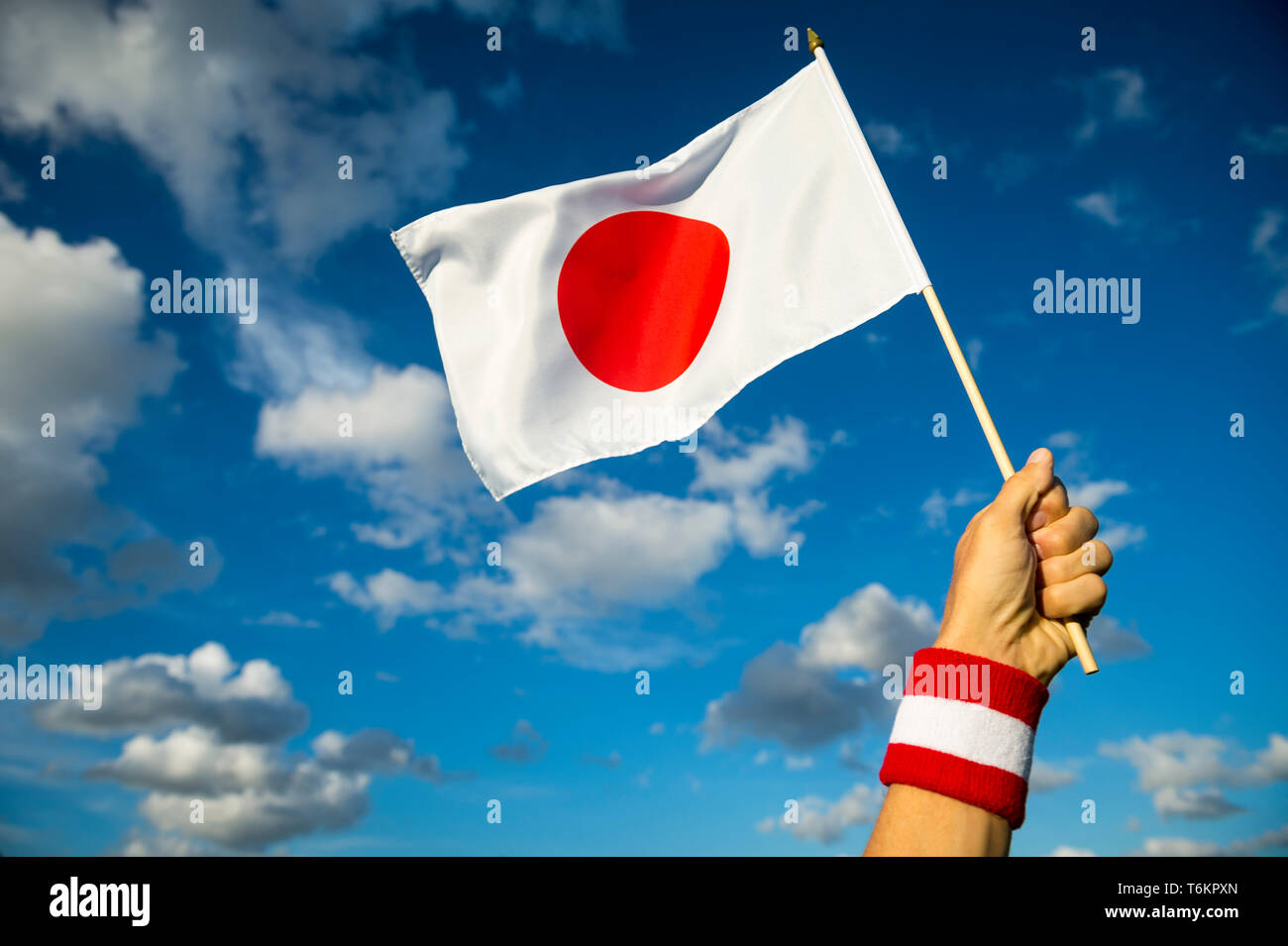 La main avec le Japon bracelet rouge et blanc tenant un drapeau japonais en bright sunny blue sky Banque D'Images