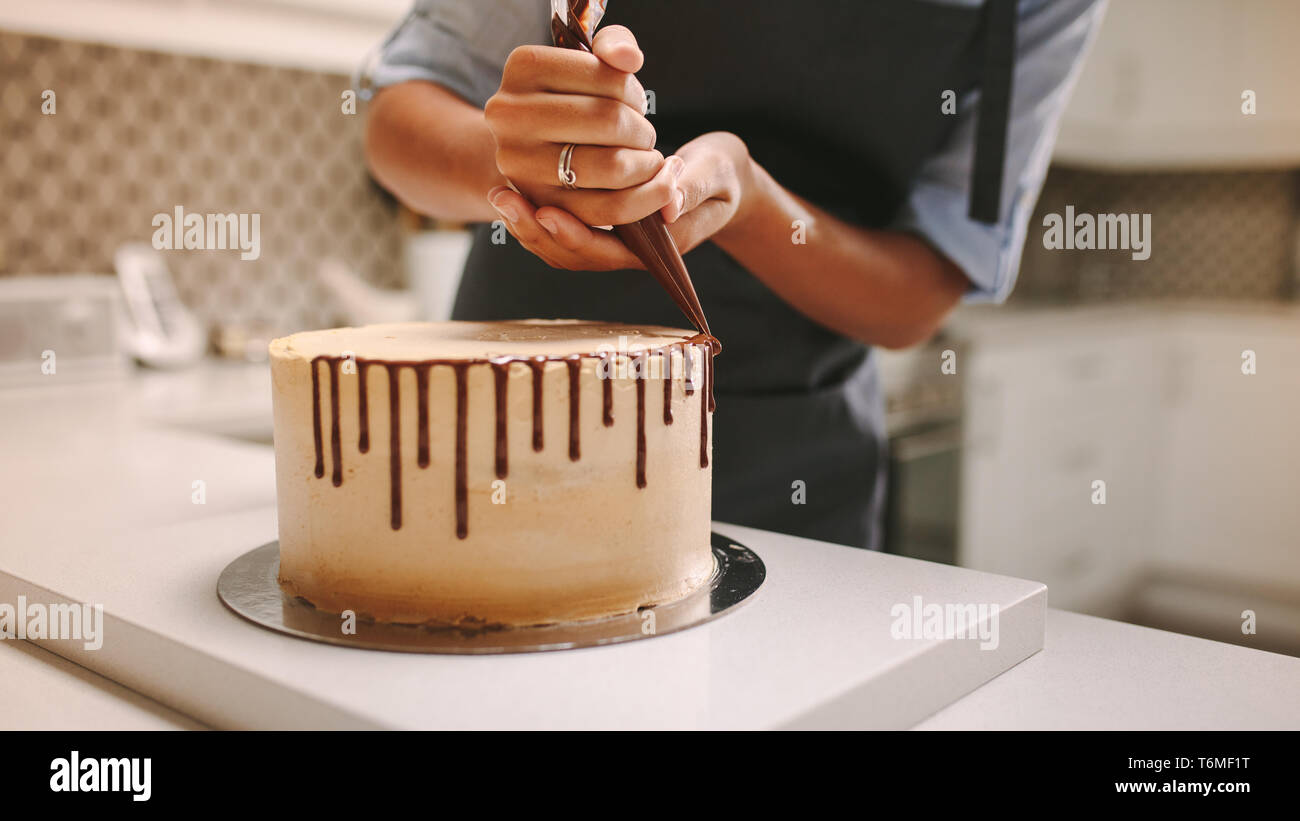 Close up of hands of a female chef avec sac confiserie chocolat liquide presser sur le gâteau. Pastry chef decorating un gâteau dans la cuisine. Banque D'Images