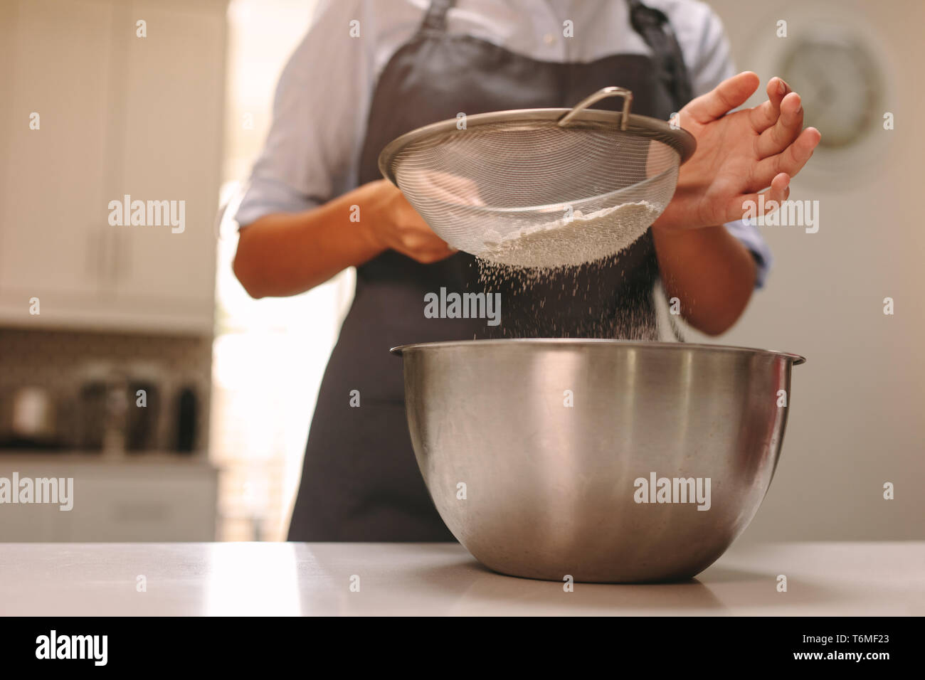 Close up of female chef pâtissier tamisant la farine dans un bol pour faire de la pâte en cuisine. La cuisson à femme baker accueil cuisine. Banque D'Images