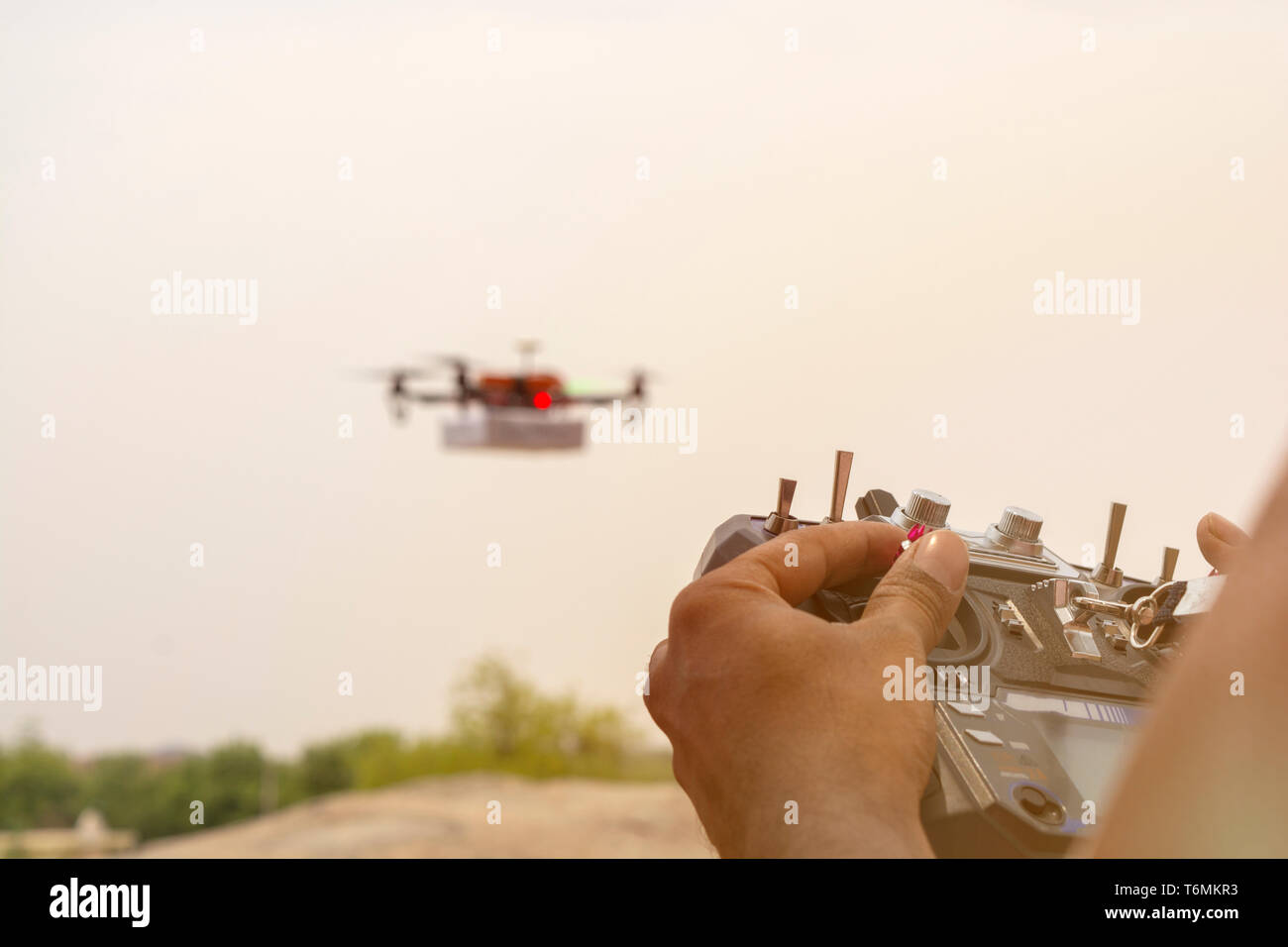 Closeup of hands opertaing drone émetteur, récepteur, contrôleur contrôleur à l'accent alors que bourdon est en dehors de la vue en arrière-plan. Banque D'Images