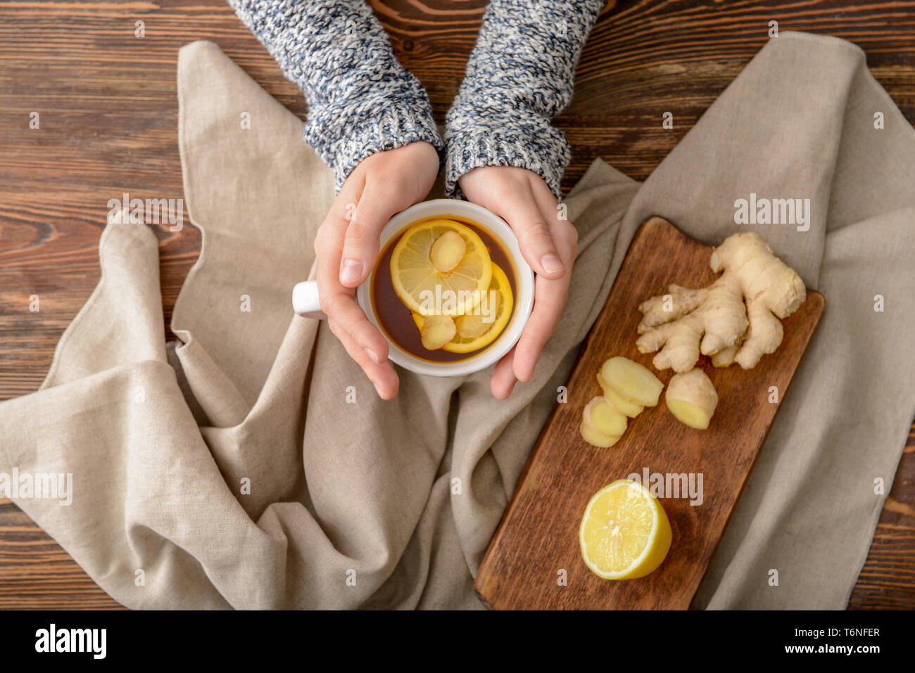 Femme tenant une tasse de thé au citron et gingembre sur table en bois Banque D'Images