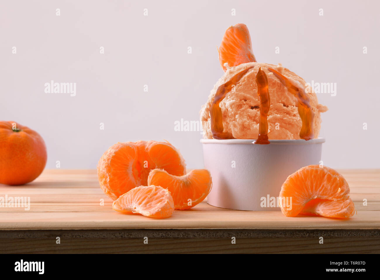 La crème glacée Mandarin tasse décorée avec des segments de mandarines sur une table en bois. Composition horizontale. Vue de face. Banque D'Images