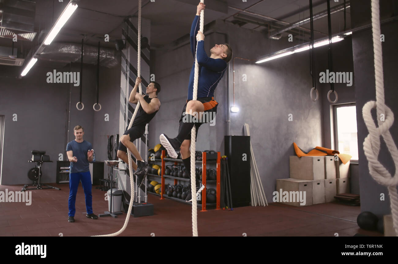 Les jeunes hommes sportifs escalade sur corde en salle de sport Banque D'Images