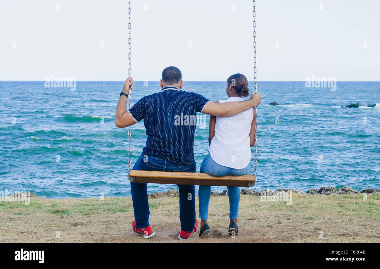 Couple assis sur une balançoire en contemplant le bleu de la mer, et derrière eux un journal sentier menant à eux. Banque D'Images