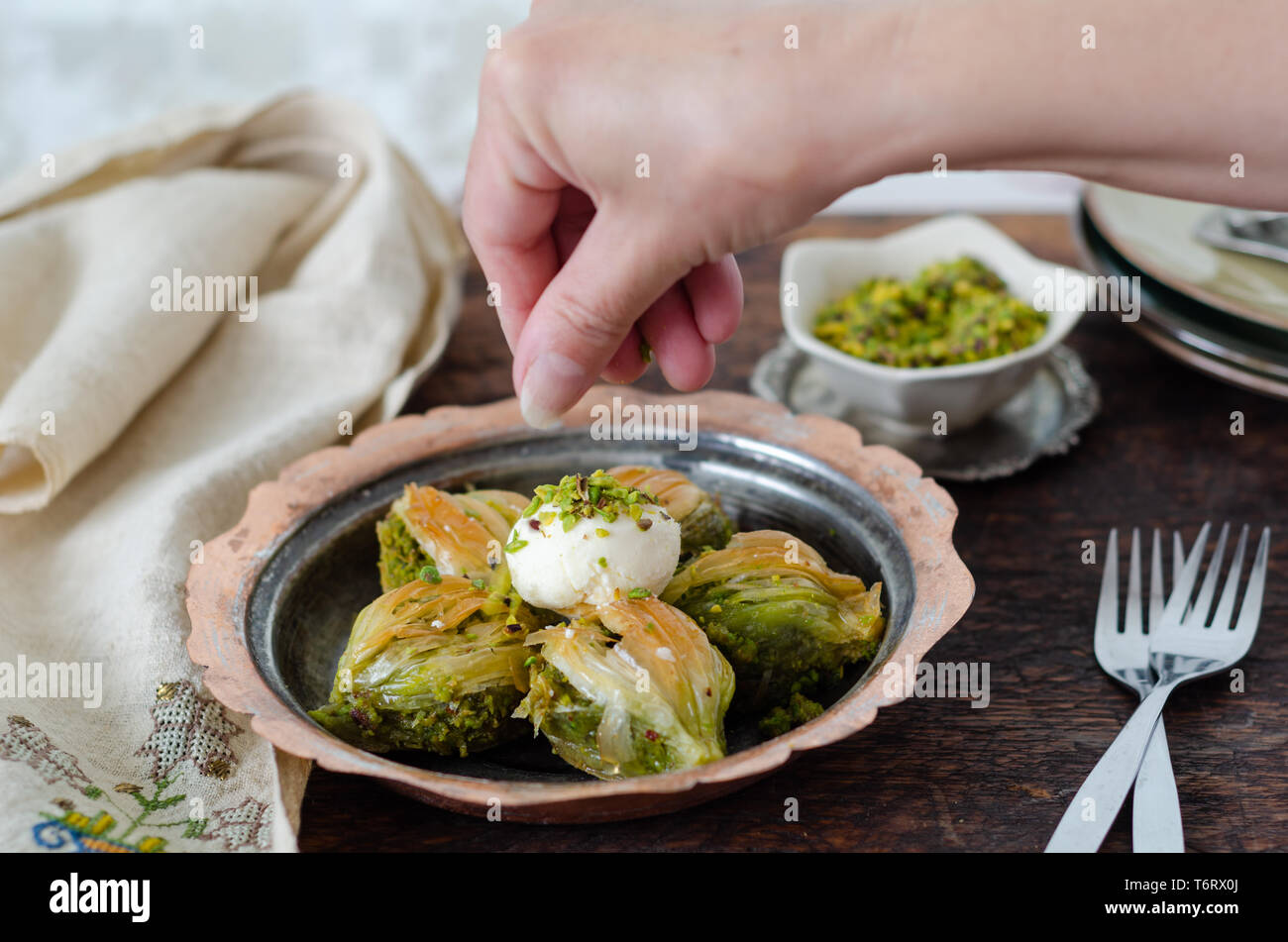 Baklava dessert turc avec la crème glacée sur la plaque de cuivre. La femme est de mettre les pistaches sur le baklava. Banque D'Images