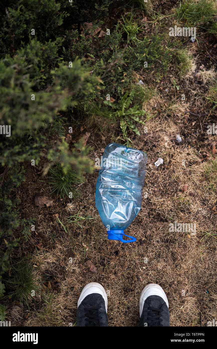 Homme trouvé debout pieds bleu - grande bouteille en plastique sur le sol dans un parc d'arbres en forêt - jeté pas recyclés - Déchets et pollution de la Banque D'Images