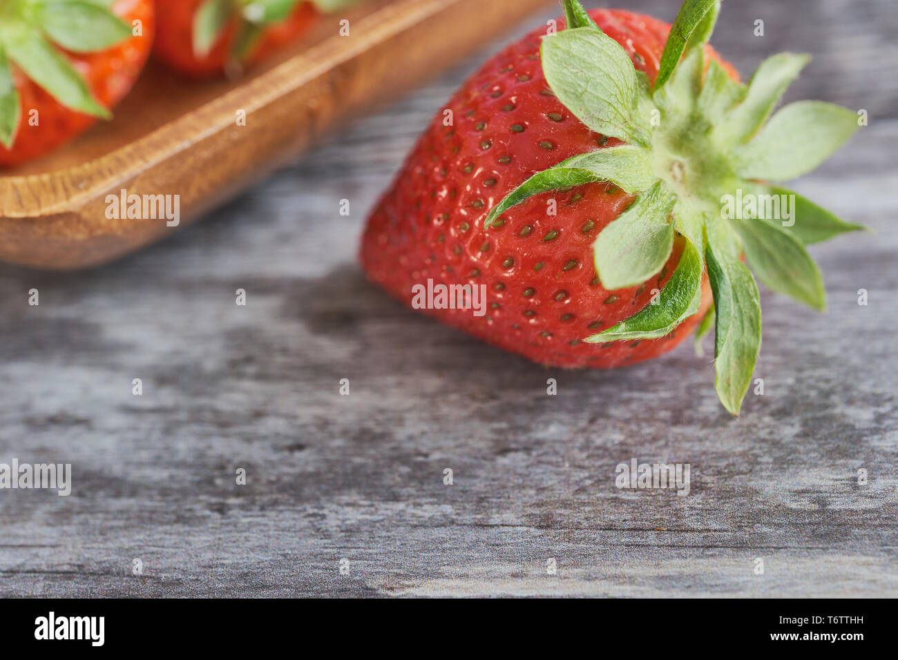 Couleur macro photo d'une seule fraise sur la surface en bois, de plus en plus floue dans l'arrière-plan est un bol en bois avec des fraises Banque D'Images