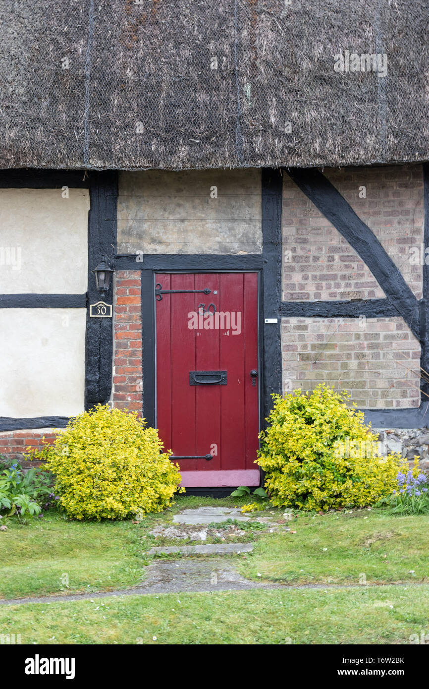 Thatched cottage anglais traditionnel avec entrée porte rouge Banque D'Images