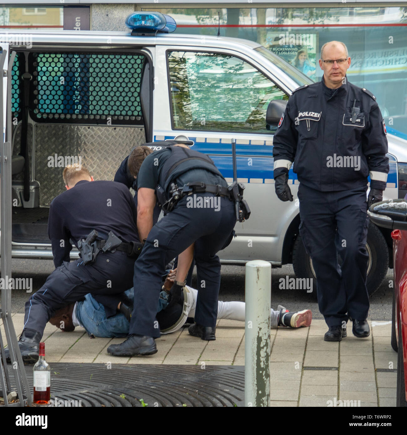 Wolfsburg, Allemagne, le 1 mai 2019 : un homme à la peau sombre est menotté par des fonctionnaires de la police en uniforme noir et tenue en bas du trottoir, Banque D'Images