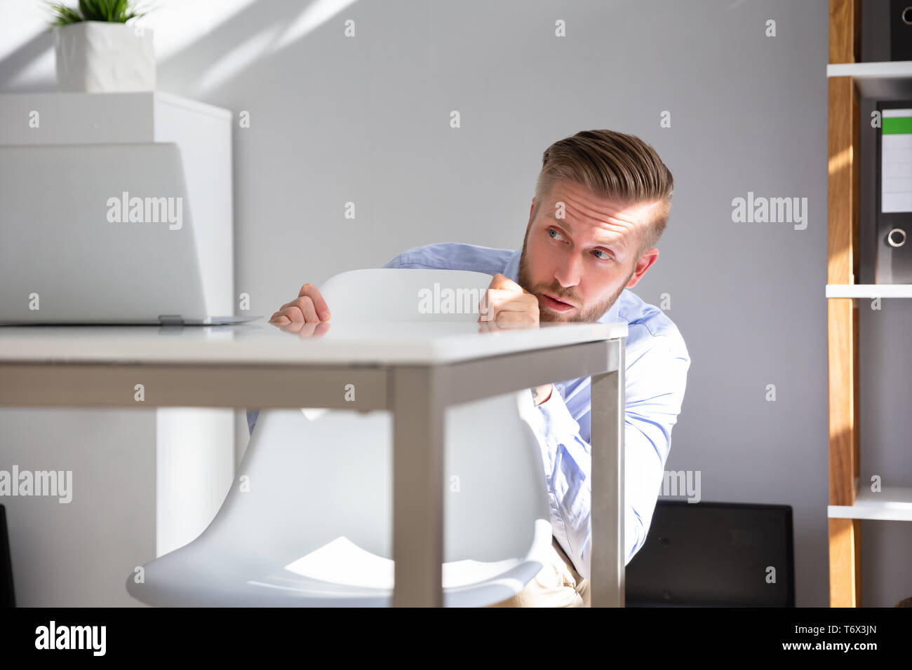 Peur Businessman Peeking du bord de Desk In Office Banque D'Images