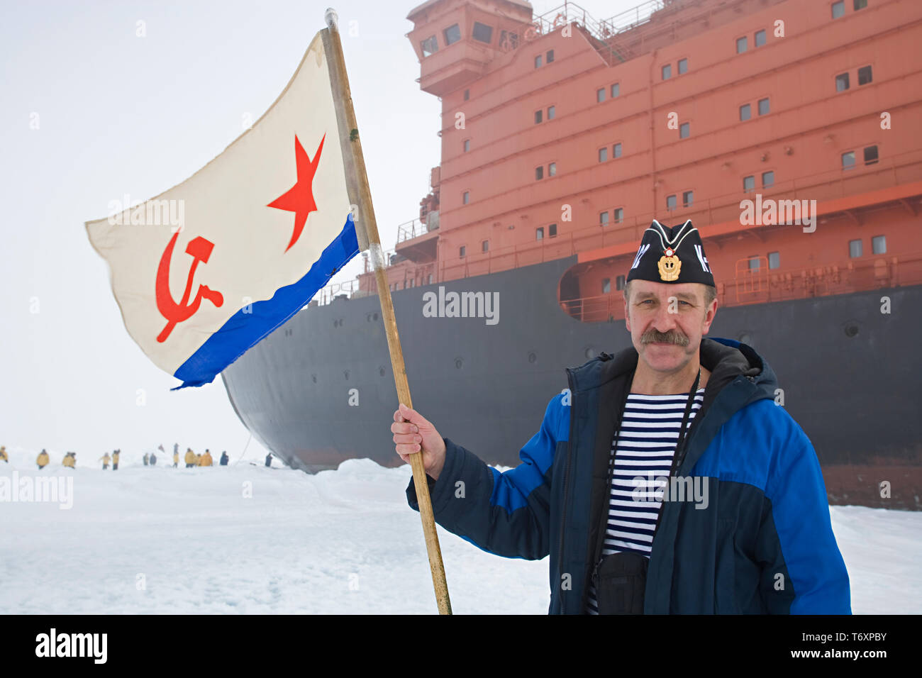 Marin russe avec drapeau soviétique debout à côté d'un brise-glace nucléaire le plus important au monde de 50 ans de la Victoire au Pôle Nord. Banque D'Images Marin russe avec drapeau soviétique debout à côté d'un brise-glace nucléaire le plus important au monde de 50 ans de la Victoire au Pôle Nord. Banque D'Images