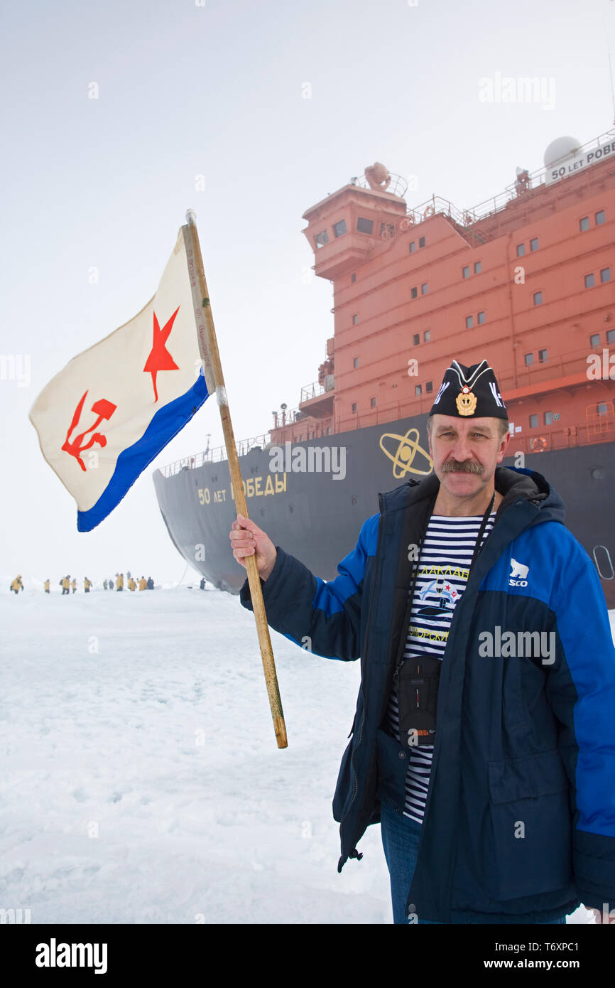 Marin russe avec drapeau soviétique debout à côté d'un brise-glace nucléaire le plus important au monde de 50 ans de la Victoire au Pôle Nord. Banque D'Images Marin russe avec drapeau soviétique debout à côté d'un brise-glace nucléaire le plus important au monde de 50 ans de la Victoire au Pôle Nord. Banque D'Images