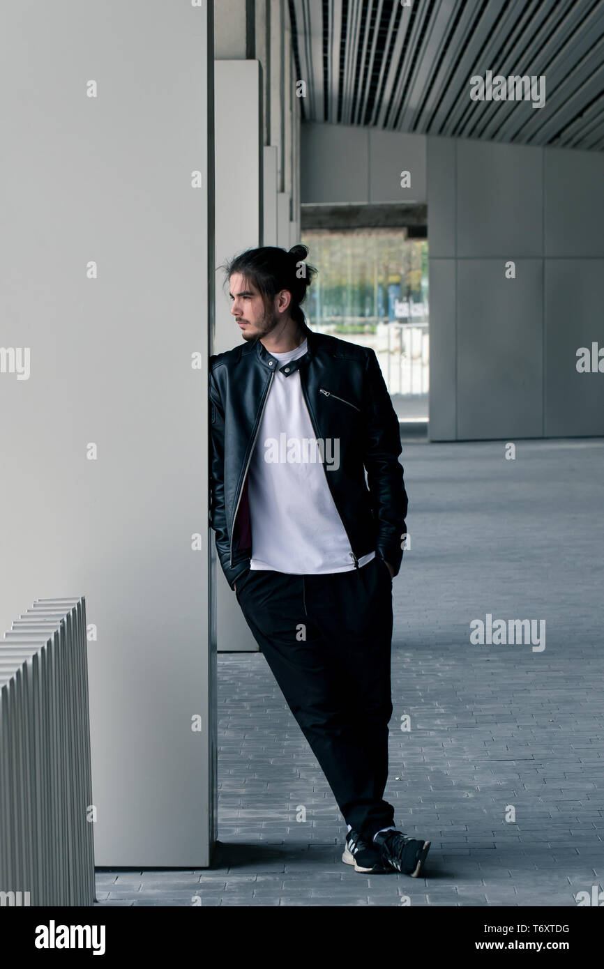 Beau jeune homme barbu dans une veste en cuir noire avec une coupe élégante et s'appuie sur le mur, à l'hôtel. Banque D'Images