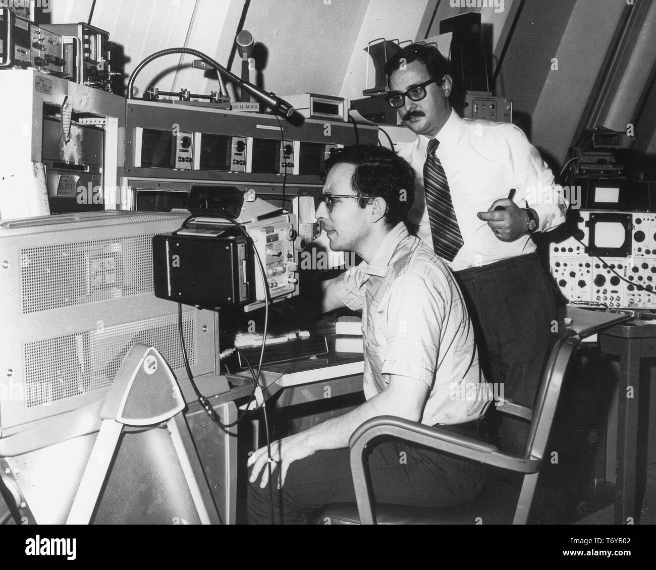 Deux chercheurs de sexe masculin, dans une pièce remplie d'équipement électrique, les travaux visant à améliorer la conception de l'accélérateur du Laboratoire Fermi, Batavia, Illinois, Mars, 1972. Image courtoisie du département américain de l'énergie. () Banque D'Images