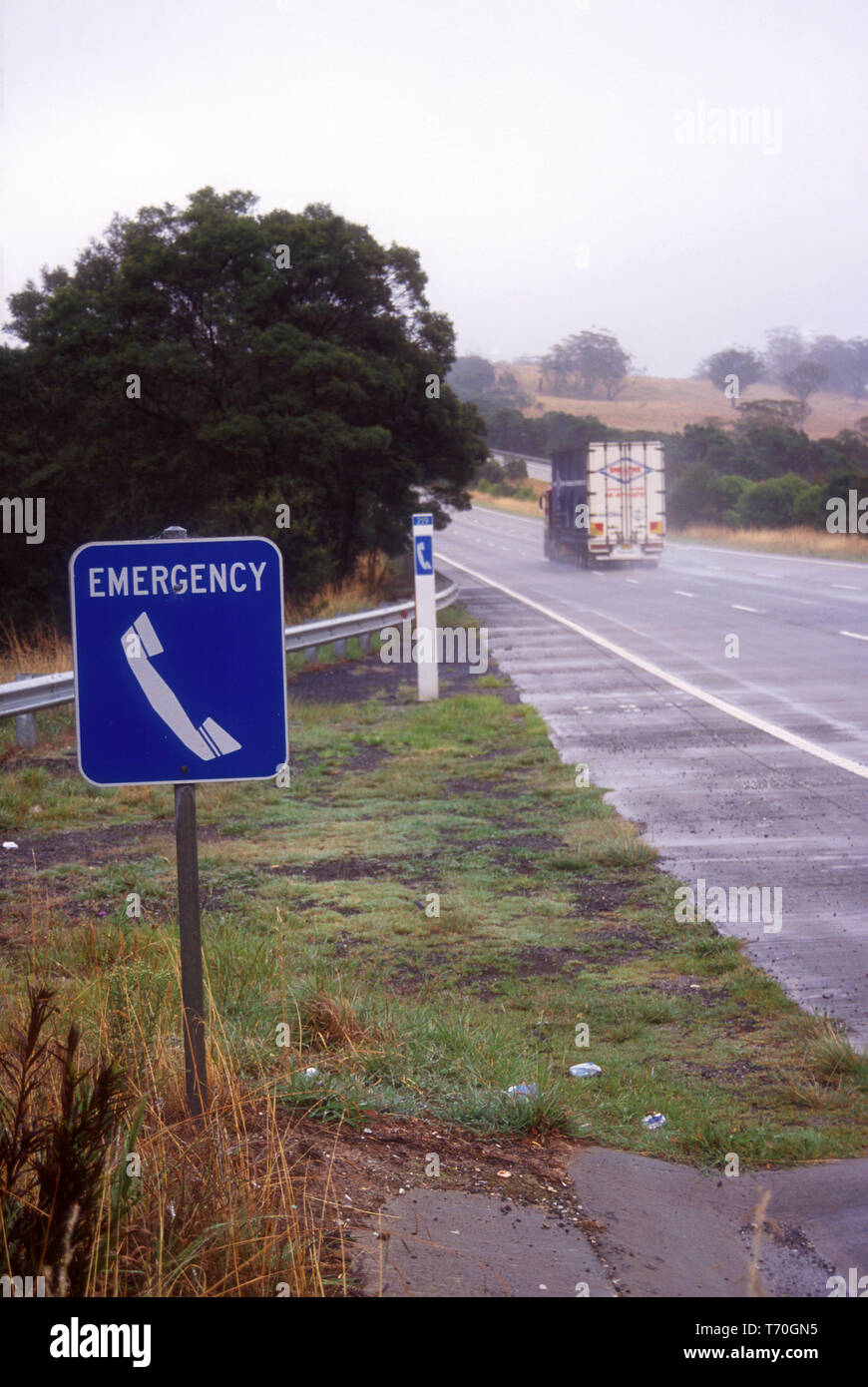 TÉLÉPHONE D'URGENCE BLEU POUR PANNE EN ARRIÈRE-PLAN UN CAMION CIRCULANT SUR UNE AUTOROUTE MOUILLE EN DIRECTION DE NEWCASTLE, NEW SOUTH WALES, AUSTRALIE. Banque D'Images