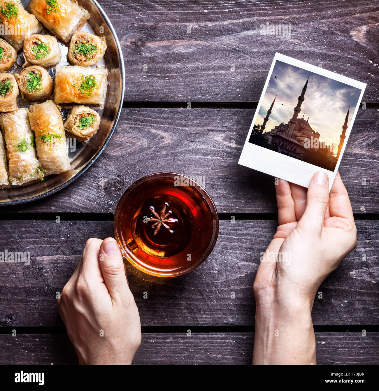 Mains avec une photo de la mosquée bleue à Istanbul et thé noir près de baklavas turcs sur fond de bois Banque D'Images