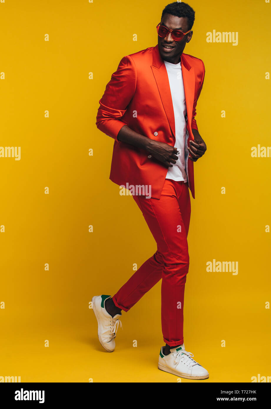 Toute la longueur du jeune homme dans l'Afrique de l'élégant costume orange sur fond jaune. Fashion model dans smart casuals. Banque D'Images