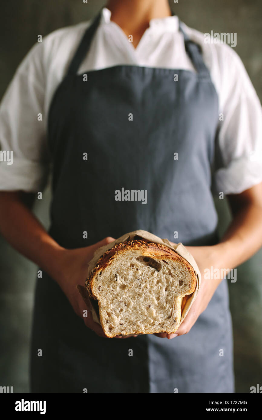 Cropped shot of female Baker en uniforme tenant du pain frais. Femme baker tenant un pain dans une boulangerie. Banque D'Images