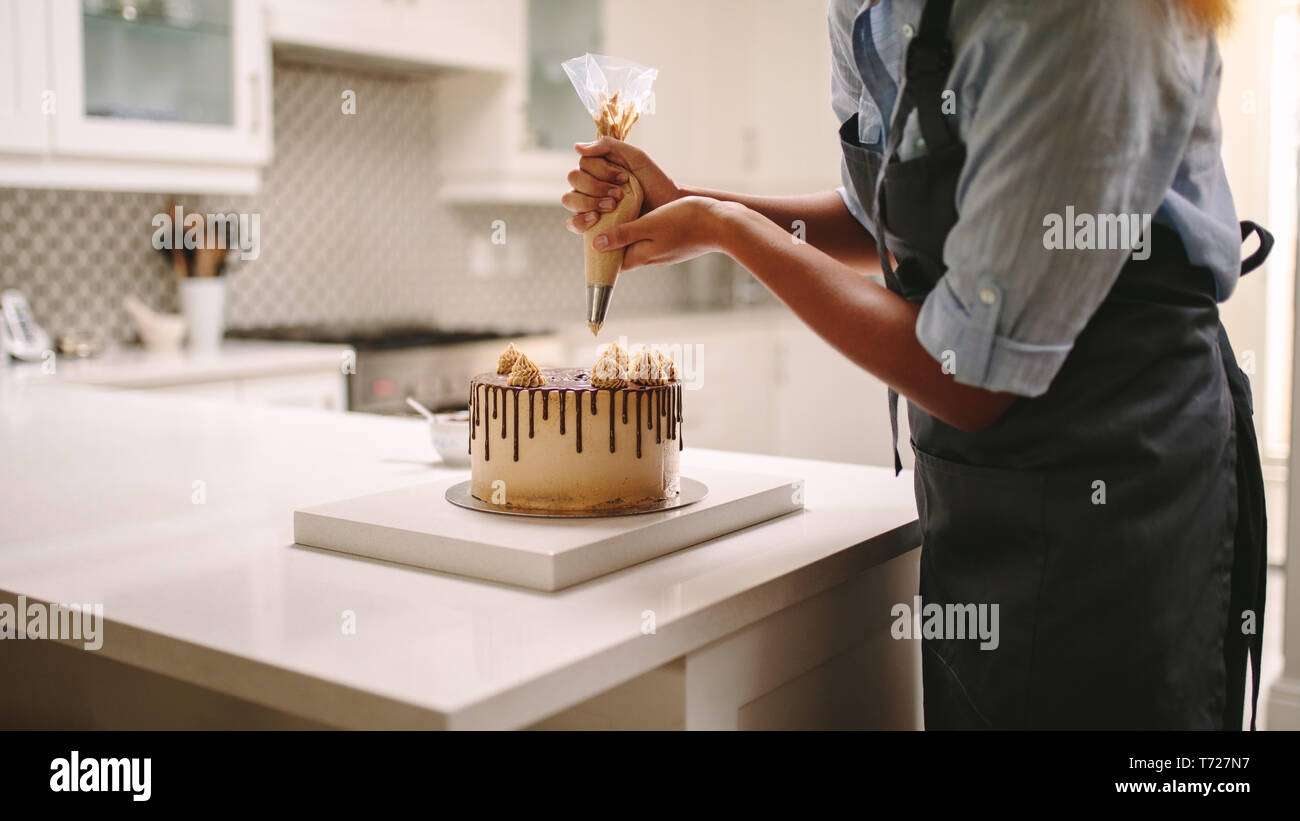 Femme chef avec poche à pâtisserie squeezing crème sur gâteau à la cuisine. On a à la maison. Banque D'Images