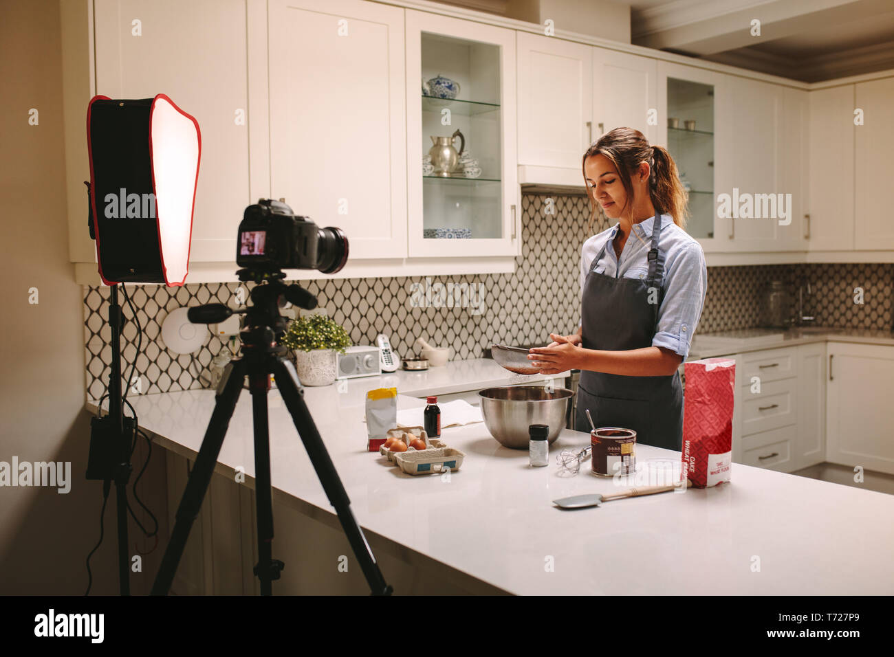 Young woman wearing apron filmer elle-même préparer des gâteaux dans la cuisine. Chef pâtissier enregistrement de contenu pour la nourriture et la cuisson à l'aide d'une caméra vidéo pe Banque D'Images