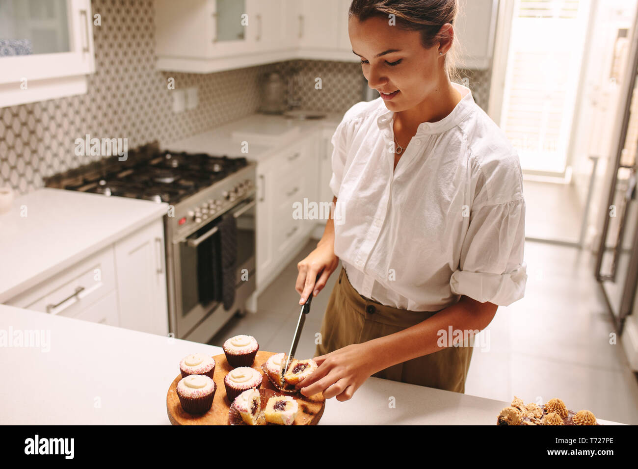 Femme debout dans la cuisine et la coupe d'un cupcake. Femme, faire un bon pâtissier pâtisserie dans la cuisine. Banque D'Images
