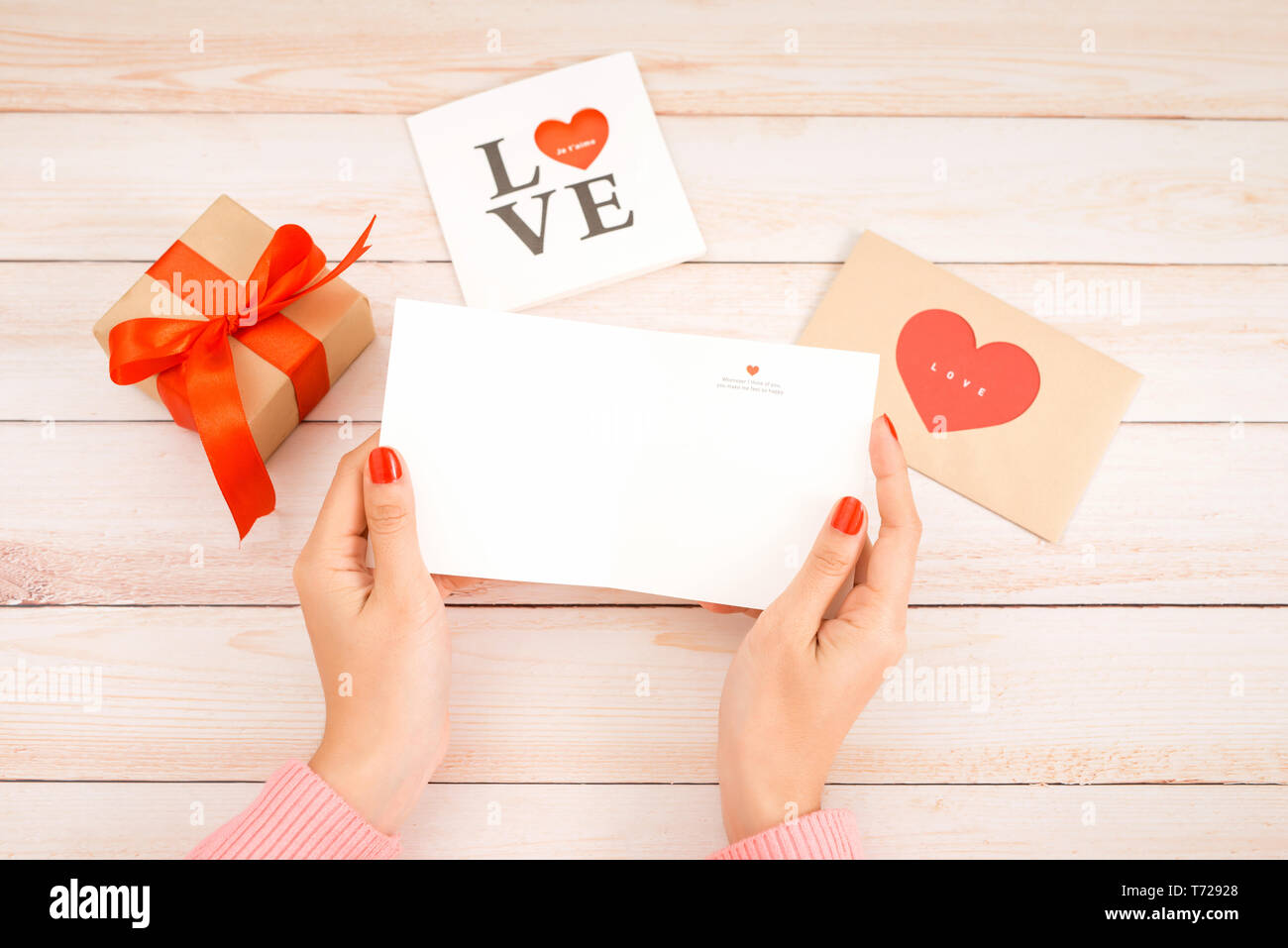 Saint-valentin lettre d'amour sur fond de bois. Les cookies en forme de coeur en velours rouge, des bonbons et du café. Les mains avec du vernis à ongles rouge Banque D'Images