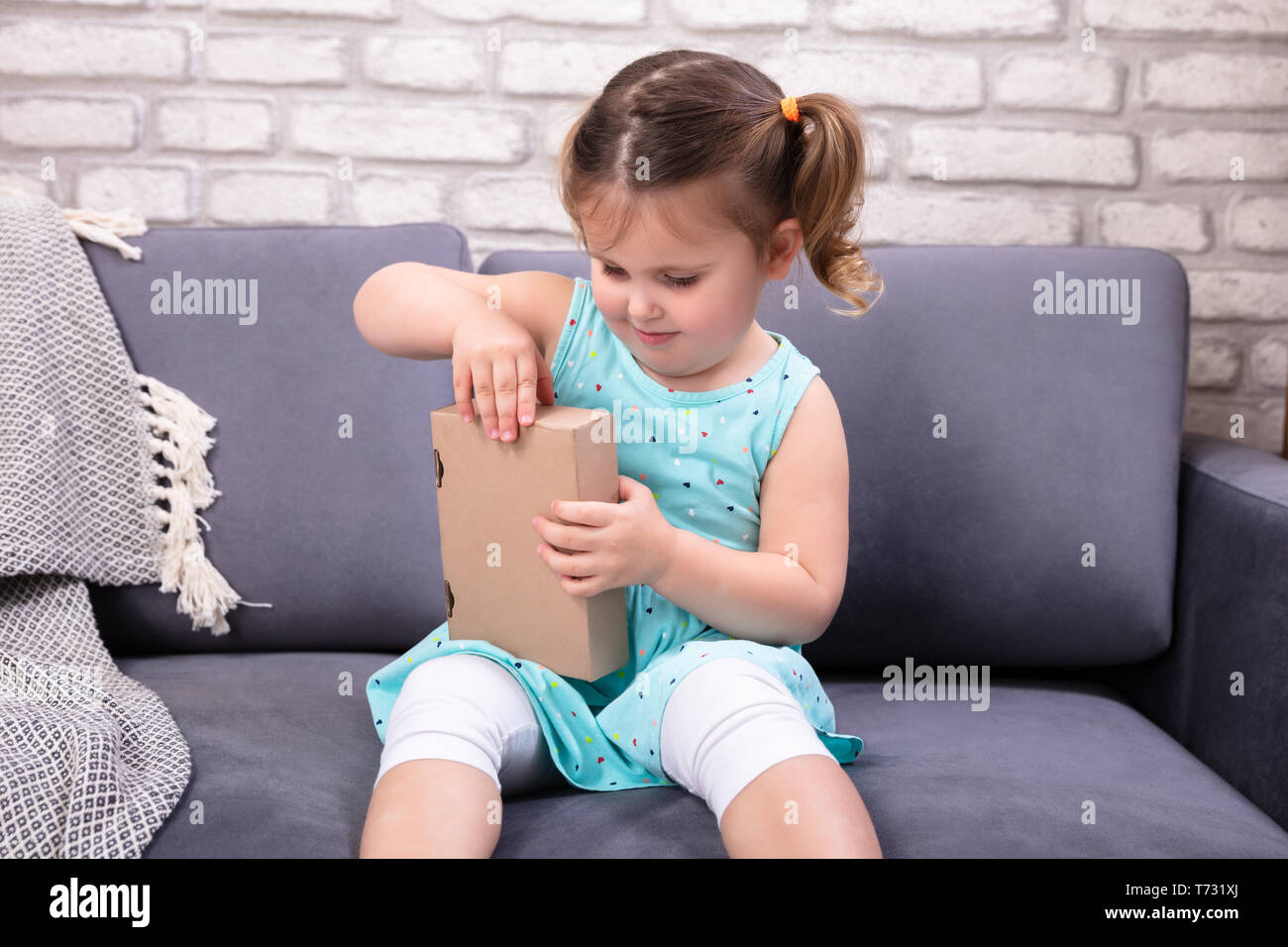 Happy Girl Sitting on Sofa ouvrant boîte à colis Banque D'Images