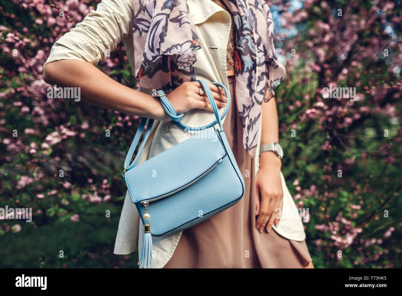 Jeune femme tenant un sac à main bleu et le port de vêtements à la mode dans le jardin. Femme printemps Vêtements et accessoires. Fashion Banque D'Images