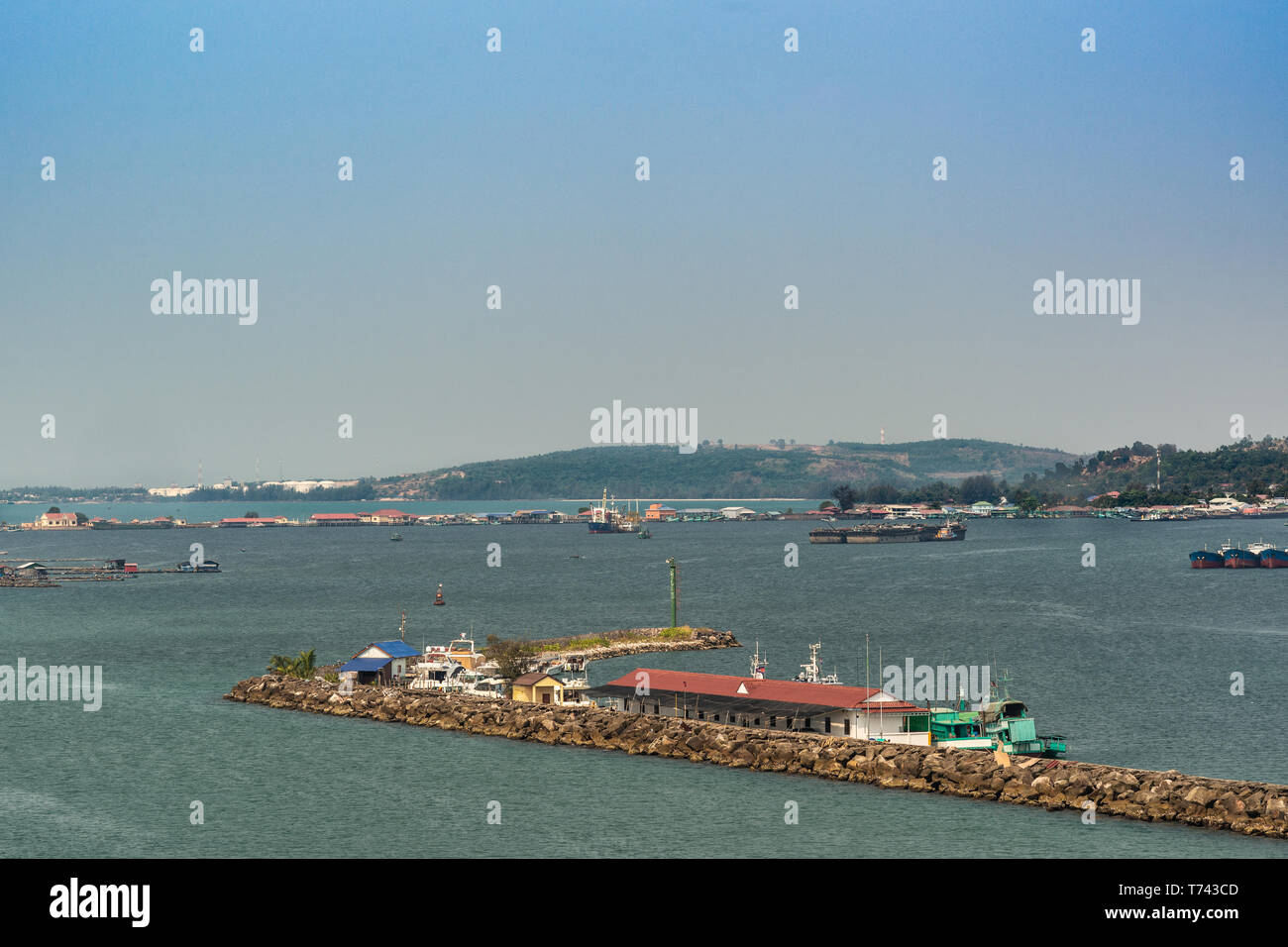 Sihanoukville, Cambodge - Mars 15, 2019 : Sihanoukville Port Autonome sous ciel bleu. Le trafic des navires et les piliers avec des bâtiments aux toits rouges. Green Hills Banque D'Images