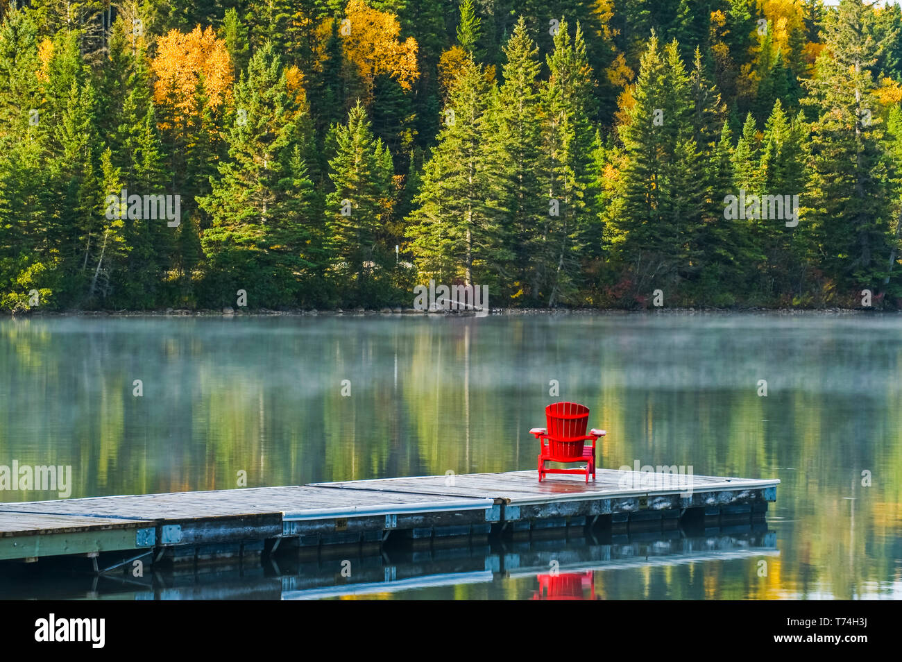 Fauteuil Muskoka sur dock à l'automne feuillage couleur reflète dans l'eau du lac tranquille de Clear Lake, parc national du Mont-Riding, Manitoba, Canada Banque D'Images