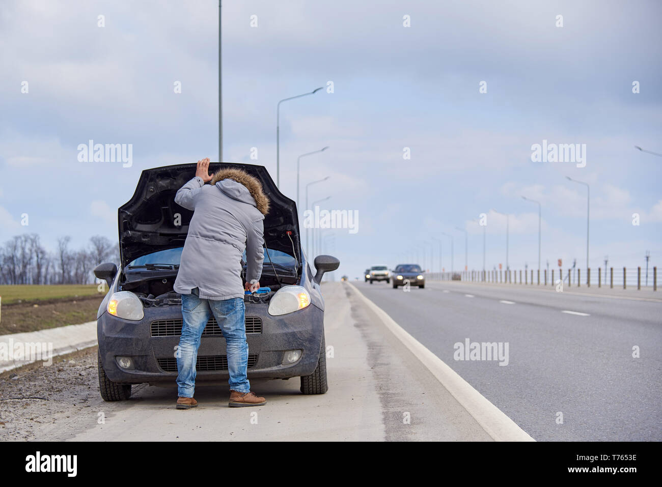 Un jeune homme près de voiture avec un capot ouvert sur le bord de la route. Banque D'Images