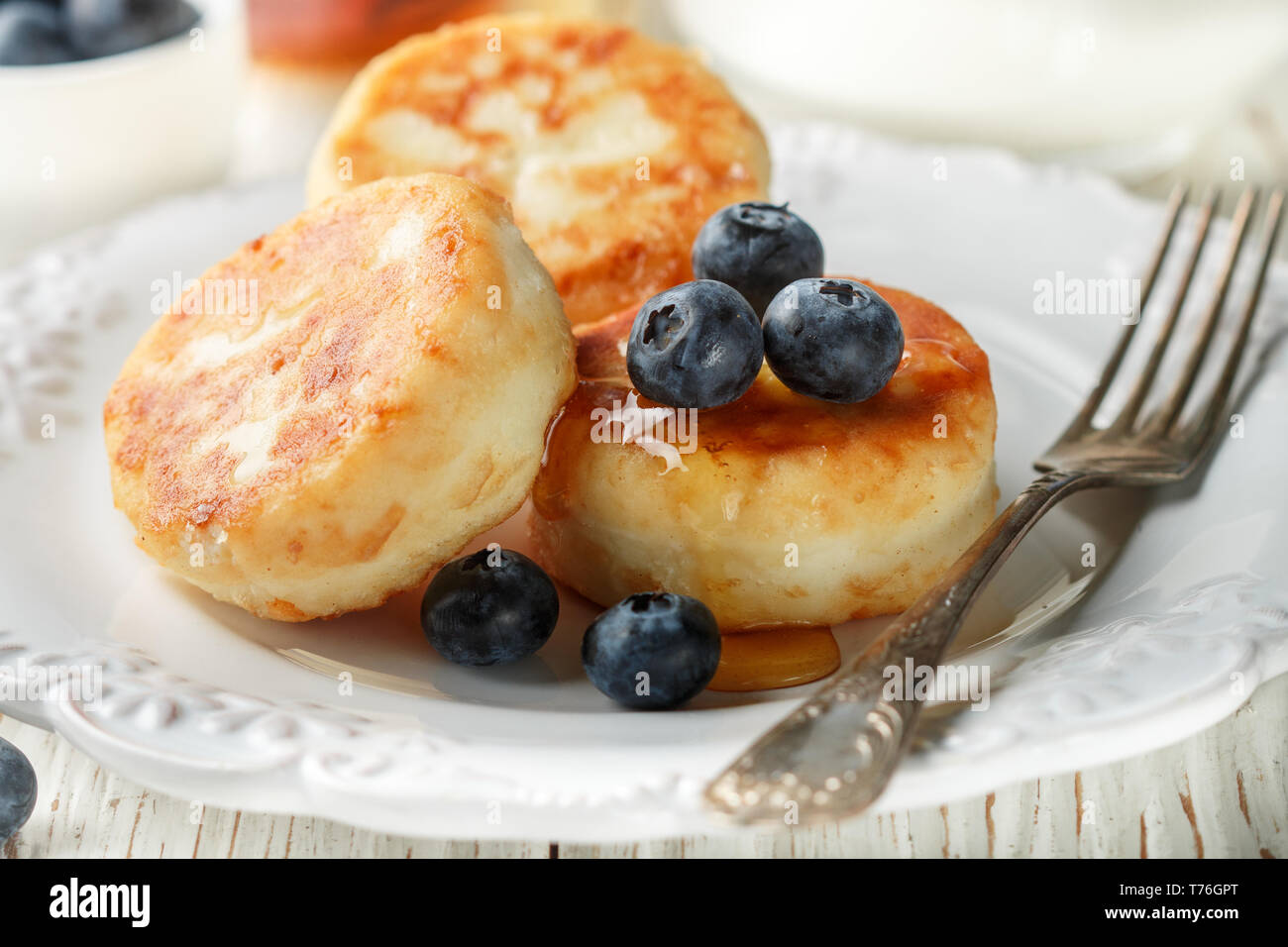 Des crêpes, du fromage cottage, fromage syrniki beignets à la myrtille baies fraîches et de miel dans une assiette blanche. Petit déjeuner gastronomique. Selective focus Banque D'Images