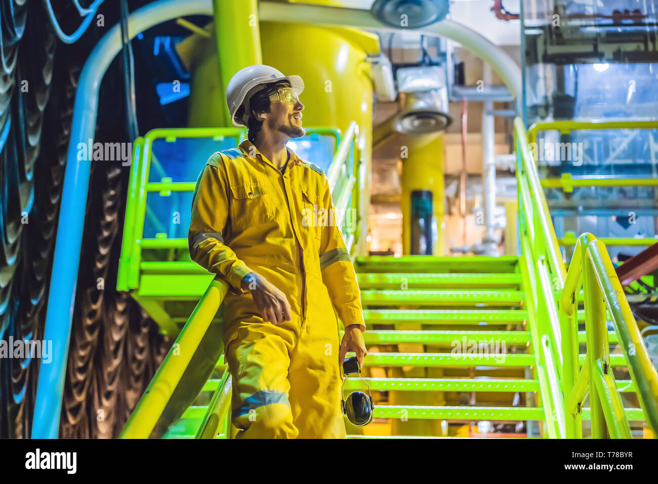 Jeune homme dans un uniforme de travail jaune, les lunettes et le casque dans un environnement industriel, plate-forme d'huile ou de gaz liquéfié plant Banque D'Images