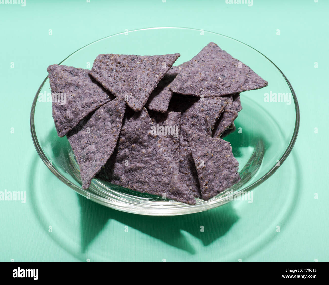 Légèrement salé Chips tortilla Maïs bleu organique dans un bol en verre clair isolé sur fond vert. Banque D'Images