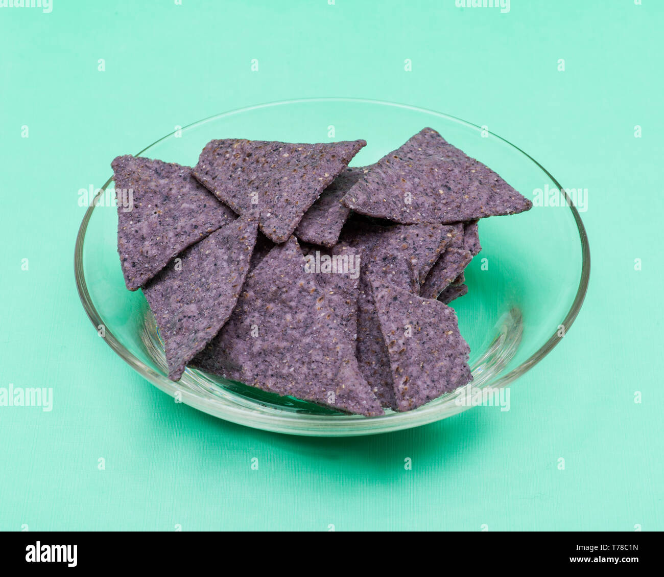 Légèrement salé Chips tortilla Maïs bleu organique dans un bol en verre clair isolé sur fond vert. Banque D'Images