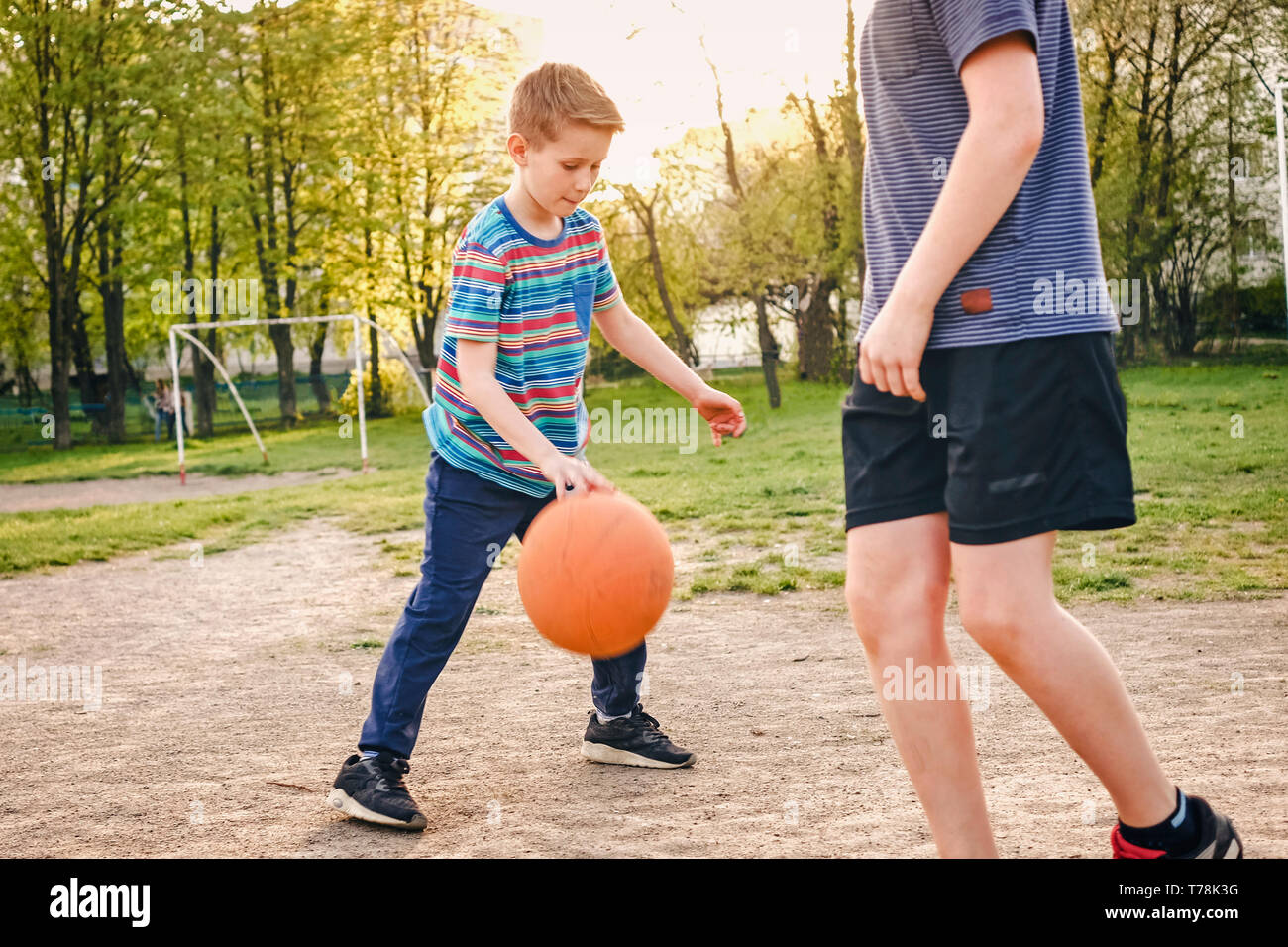 Deux jeunes garçons pratiquer leur basket-ball en plein air sur un terrain de sport en milieu rural en vue de l'un des garçons de la seconde de rebondir la balle par le contre-jour Banque D'Images