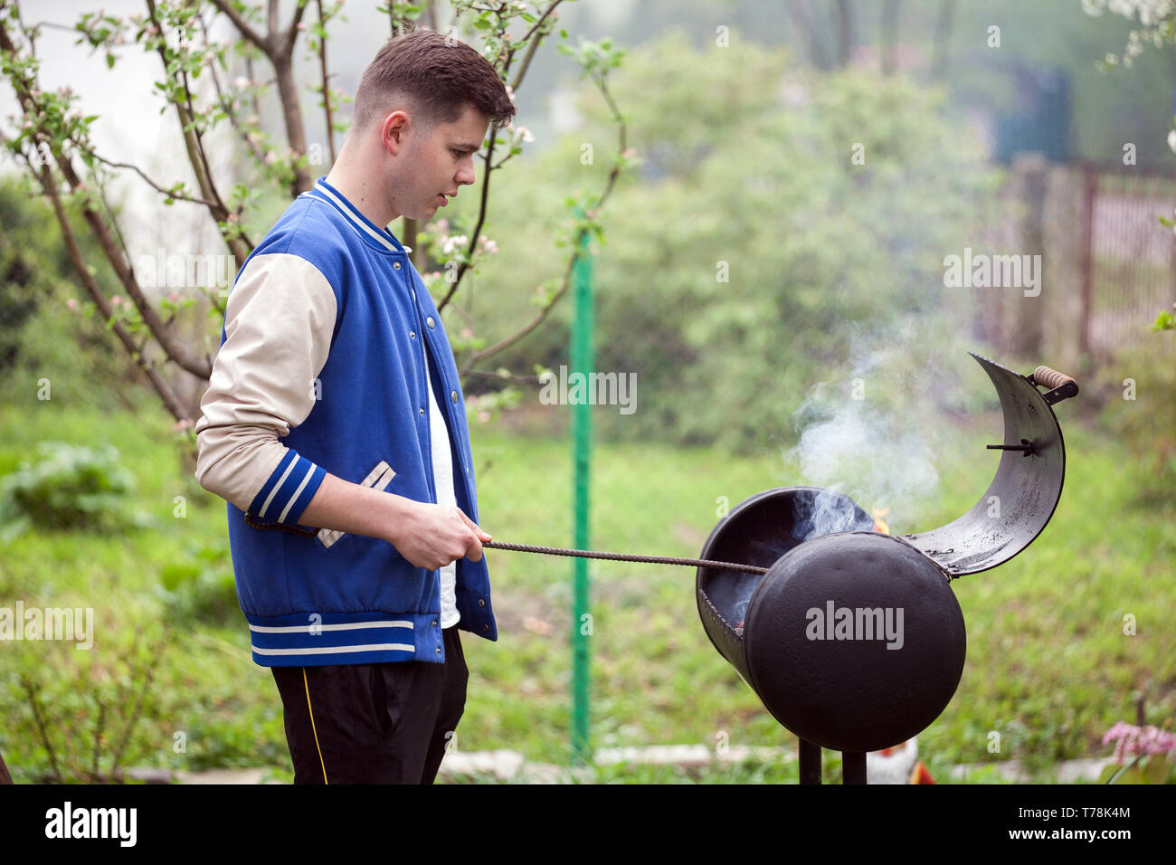 Jeune homme debout près du barbecue. Allumer le feu à l'air libre. Bel homme sportif en cour près de leur chambre se prépare un barbecue pis Banque D'Images