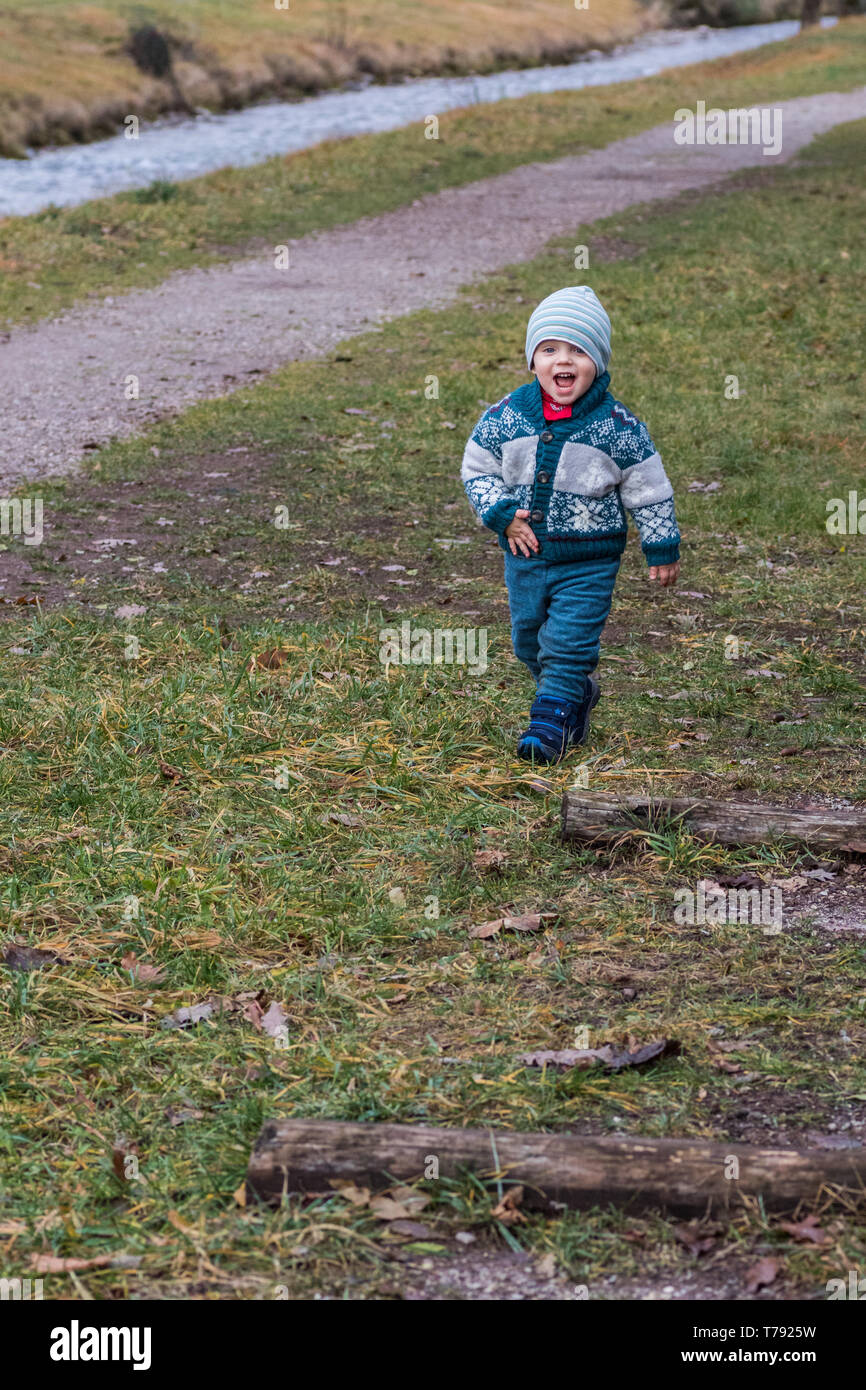 Un bambin, habillé pour la réchauffer un temps plus frais, est vu souriant joyeusement et la marche à pied. Banque D'Images