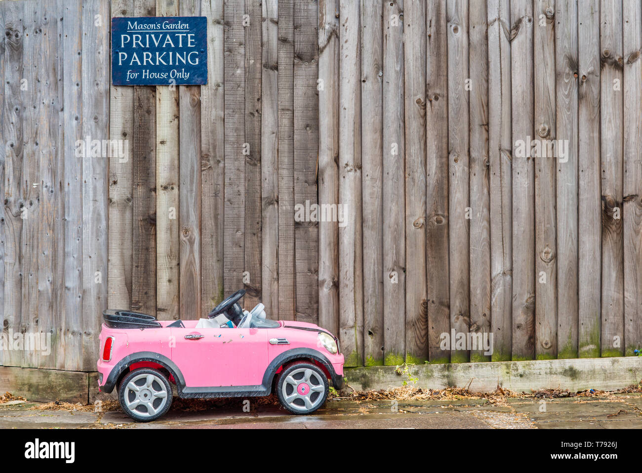 Image d'humour d'un petit jouet enfant voiture garée en dessous d'un parking privé. Vu à Cambridge, Angleterre, Royaume-Uni. Banque D'Images