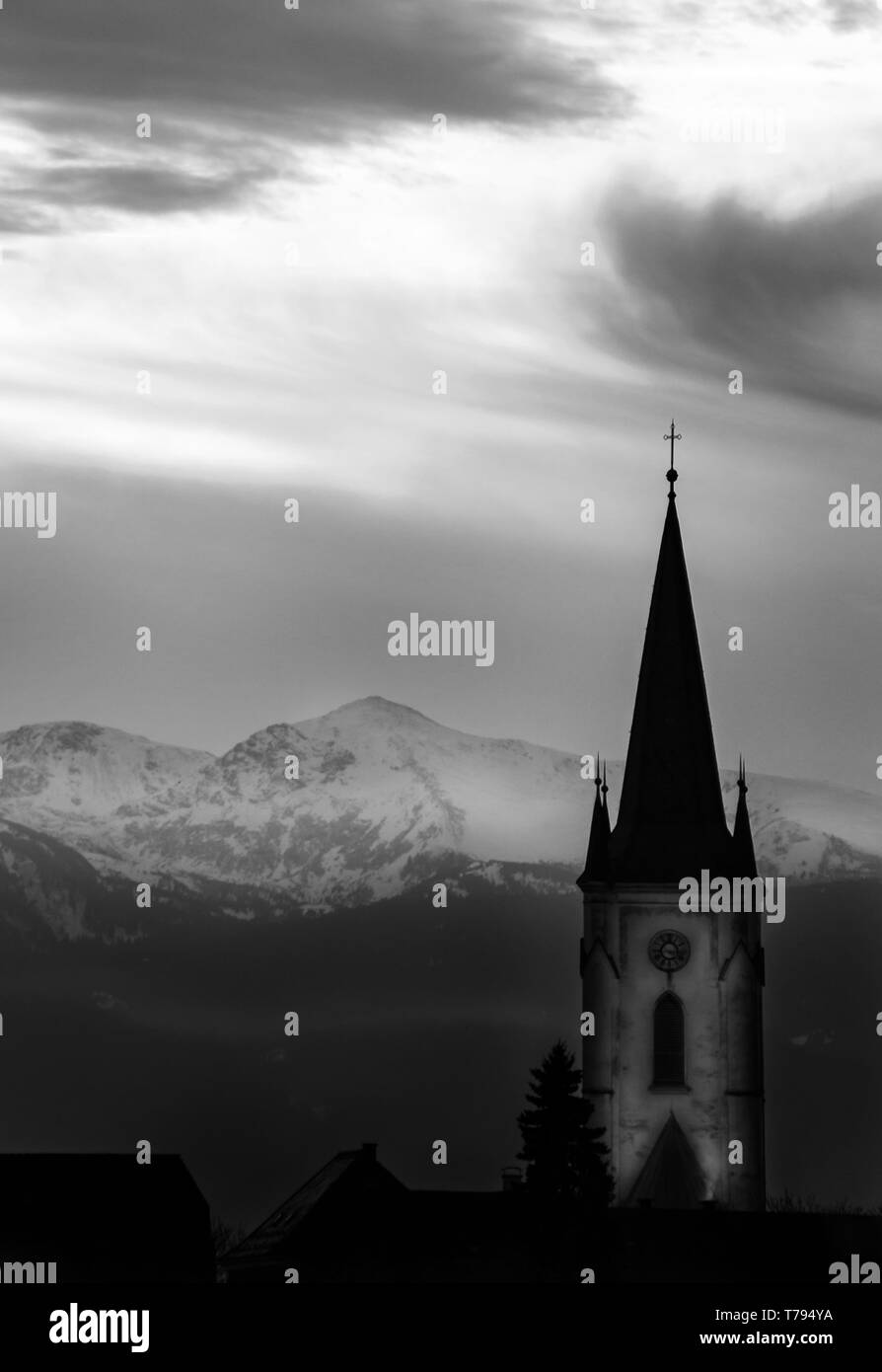 Coucher de soleil dans un paysage mystique brumeux avec des nuages et une silhouette de montagne avec un tour de l'église dans les Alpes autrichiennes Banque D'Images