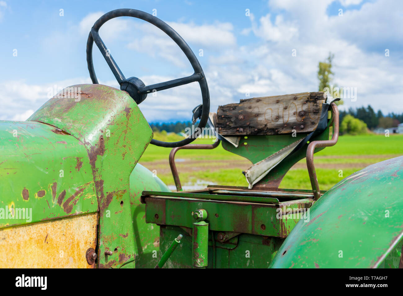 Vieux siège du tracteur dans une ferme. Montre la roue en bois et la sauvegarde. Vieux vert et jaune de l'équipement agricole. Banque D'Images