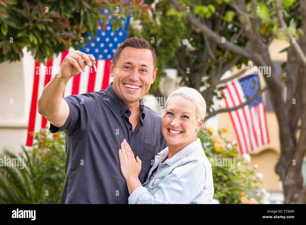 Couple heureux avec de nouvelles clés de maison en face de maisons avec des drapeaux américains. Banque D'Images