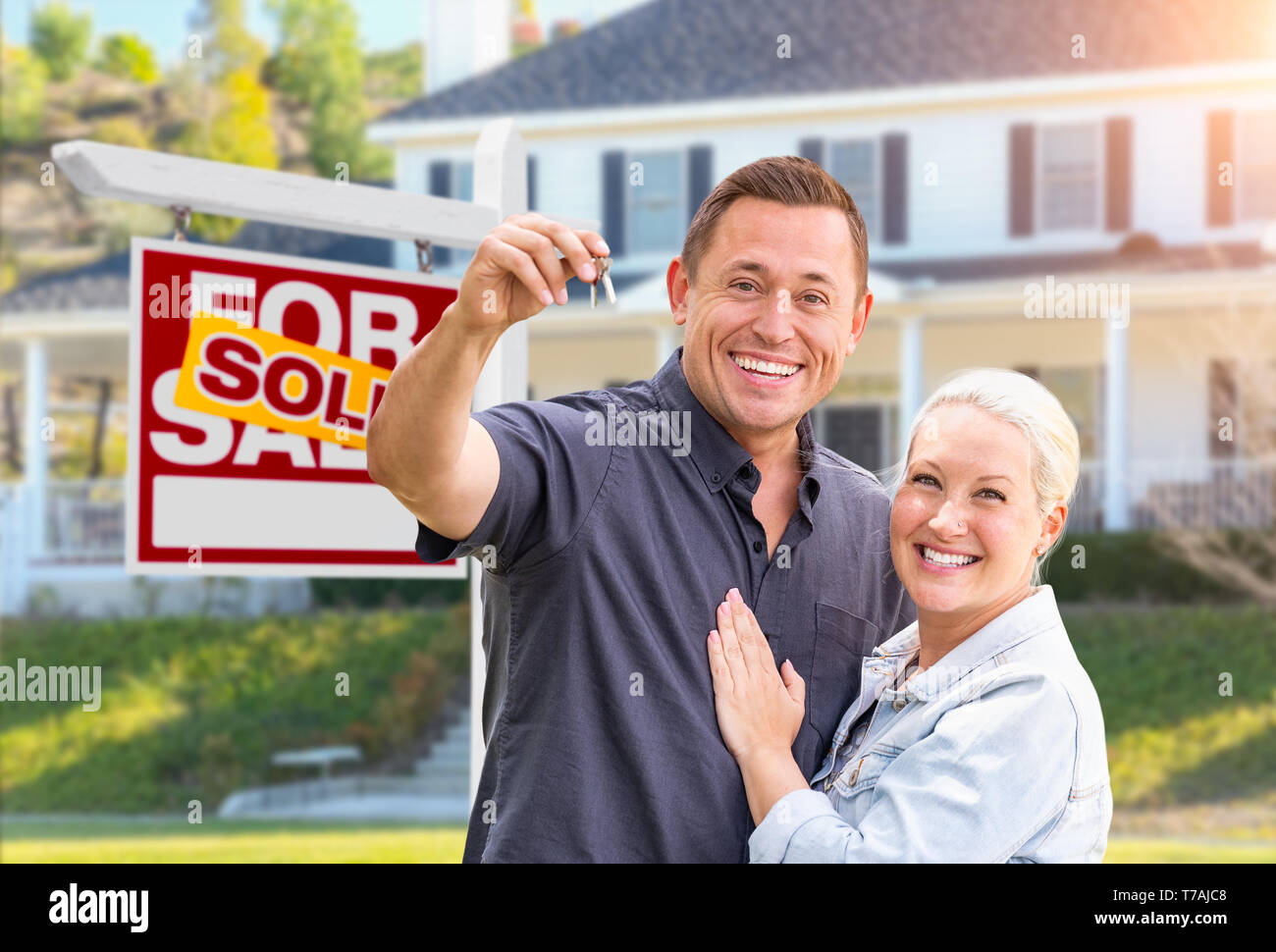 Couple heureux avec de nouvelles clés de maison en face de vendu enseigne immobilière et belle maison. Banque D'Images