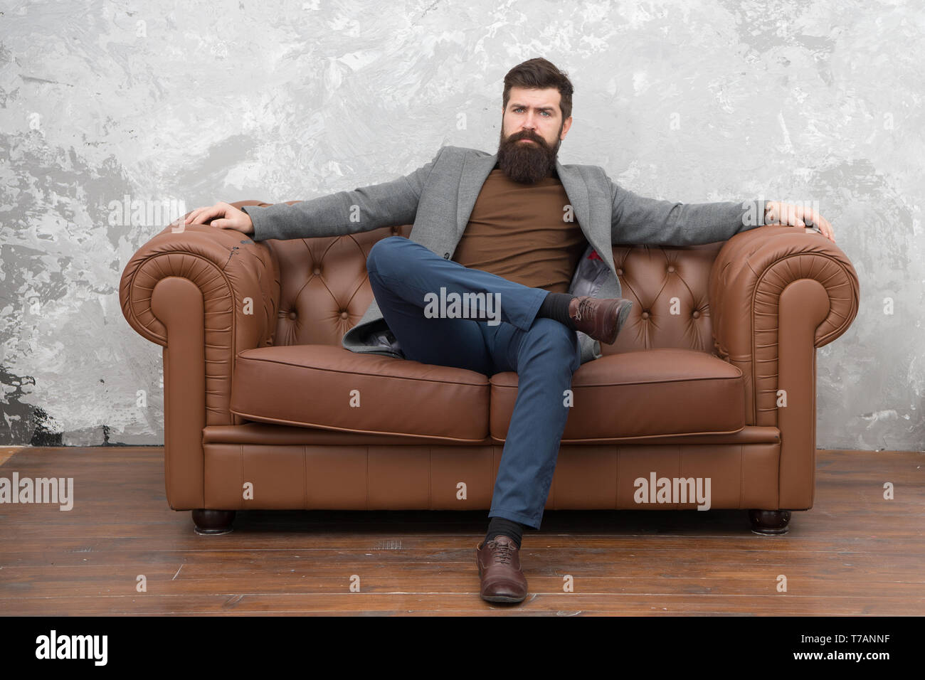 Homme barbu avec confiance s'asseoir face à un canapé en cuir. Loft appartement intérieur. Le travail de l'agent immobilier d'affaires. Boutique de meubles. Agent immobilier Hipster style loft. Agent immobilier et location de vélos. Louer appartement. Banque D'Images