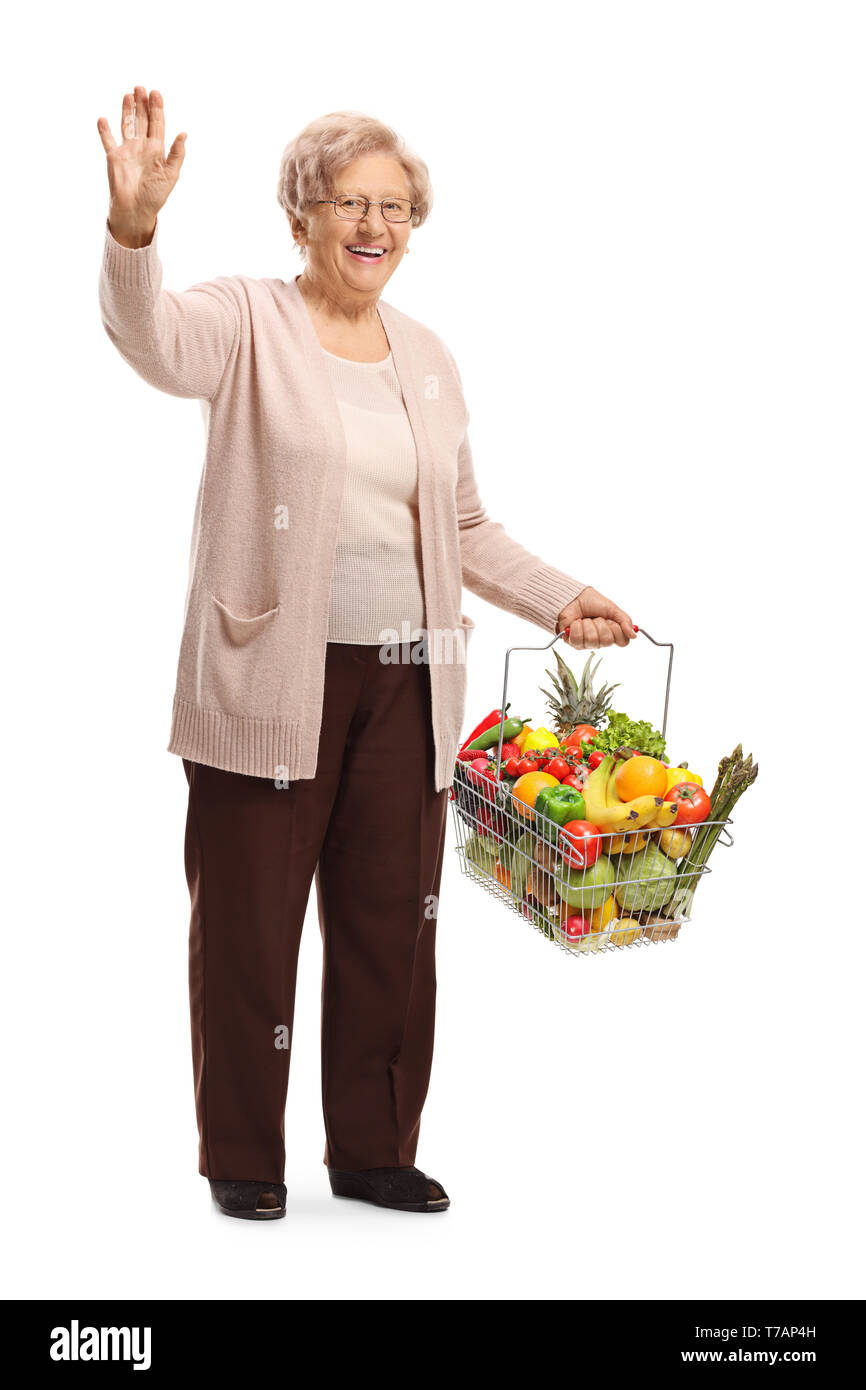 Portrait d'une femme âgée avec des fruits et légumes dans un panier en agitant sa main isolé sur fond blanc Banque D'Images