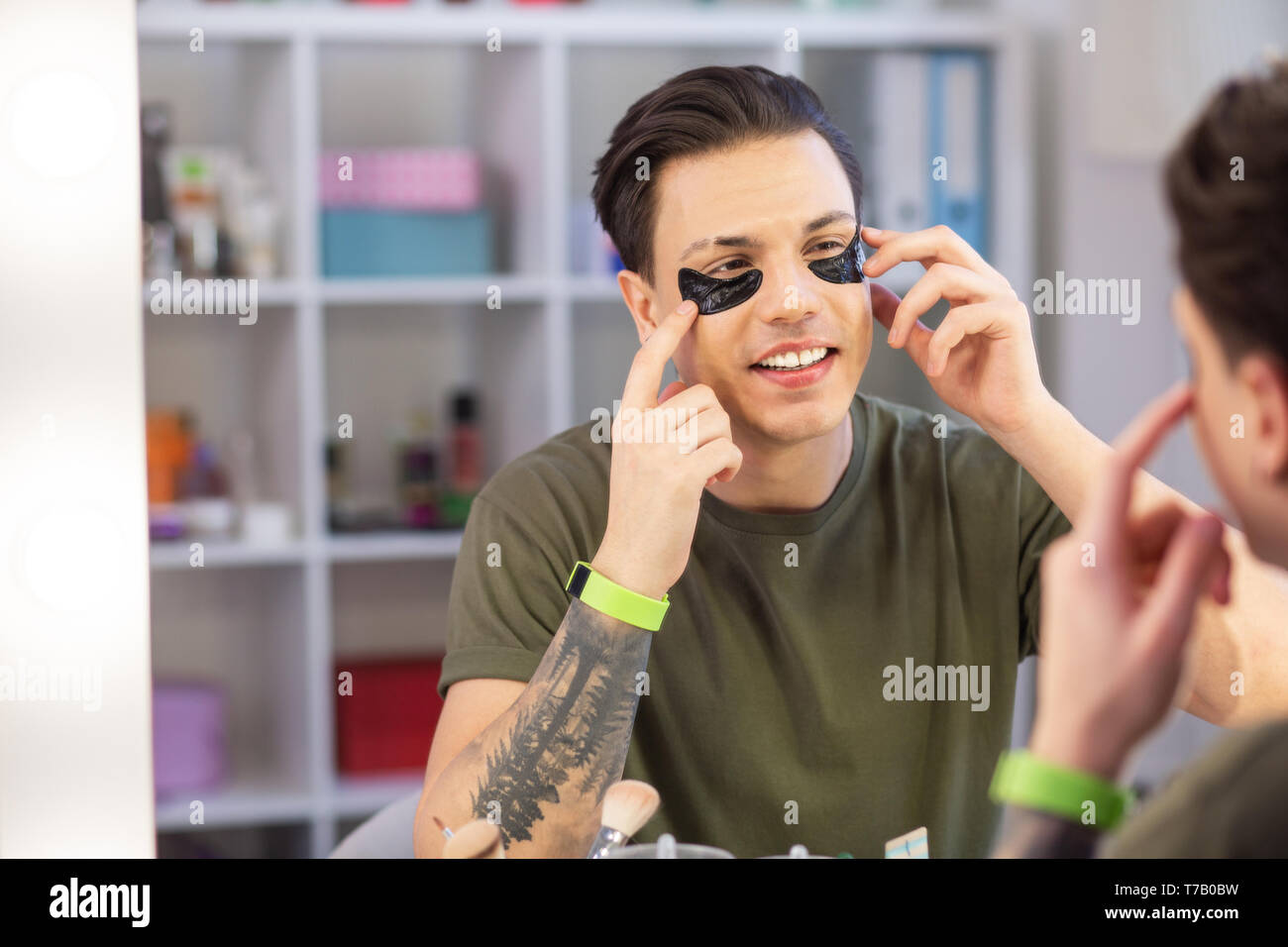 L'homme souriant avec les yeux bruns dans la région des yeux hydratant Banque D'Images