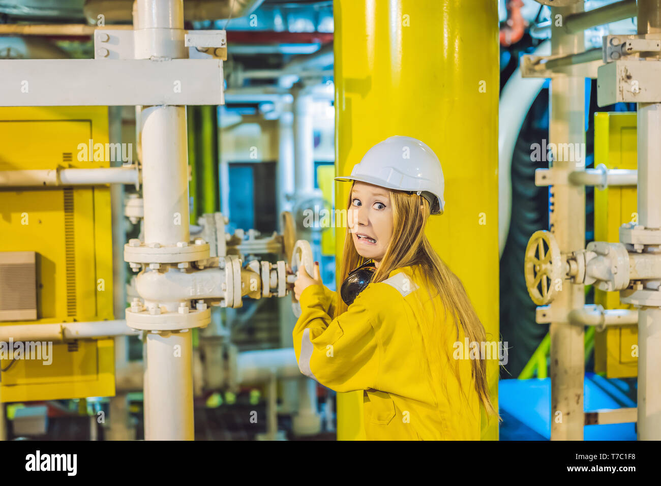 Jeune femme en uniforme de travail jaune, les lunettes et le casque dans un environnement industriel, plate-forme d'huile ou de gaz liquéfié plant Banque D'Images