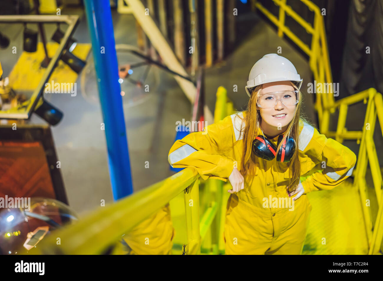 Jeune femme en uniforme de travail jaune, les lunettes et le casque dans un environnement industriel, plate-forme d'huile ou de gaz liquéfié plant Banque D'Images
