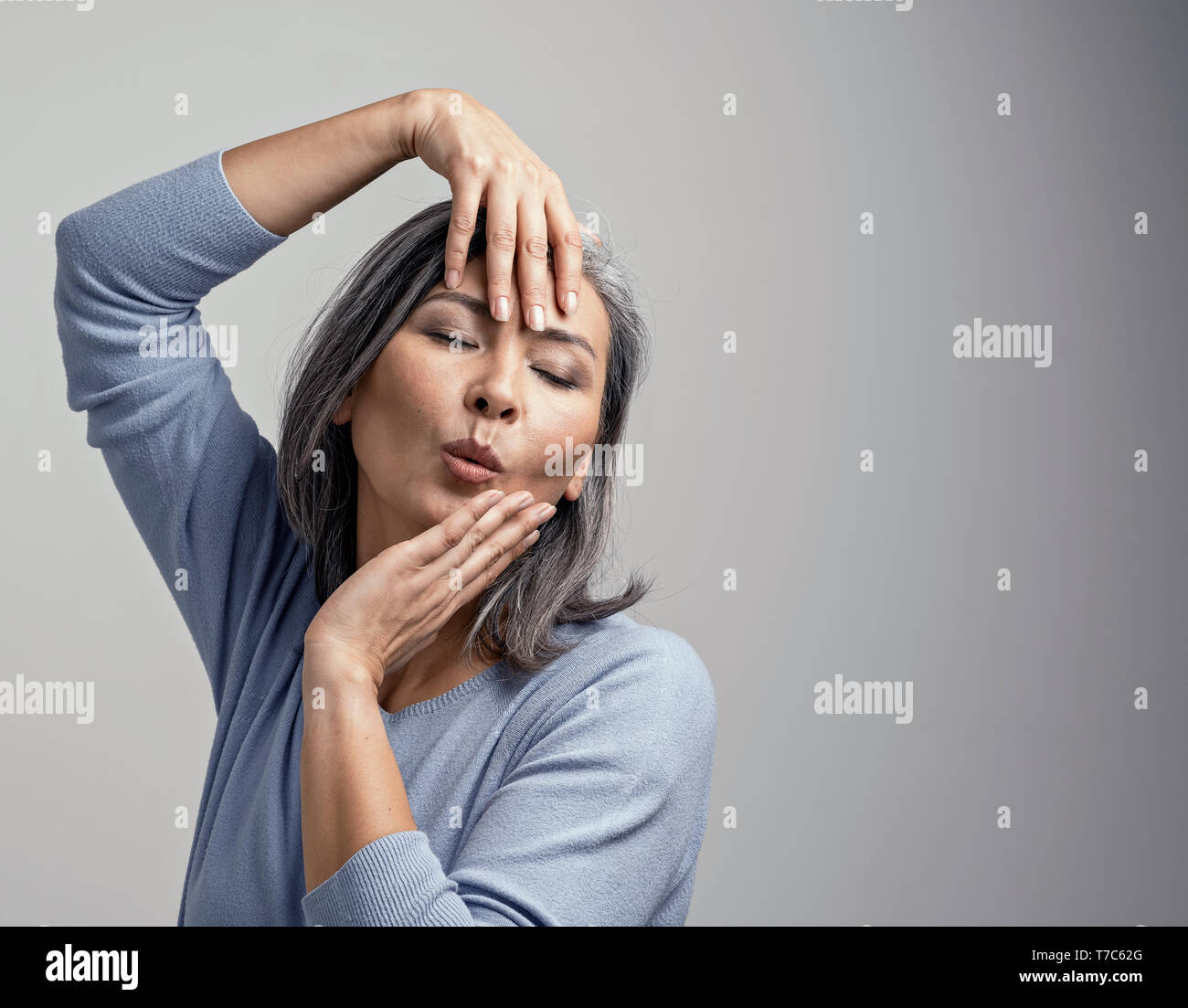 Bel Gray-Haired modèle féminin pose pour la caméra. Charmant Middle-Aged Woman Touching Her face avec les mains tout en se posant à la photo Stud Banque D'Images