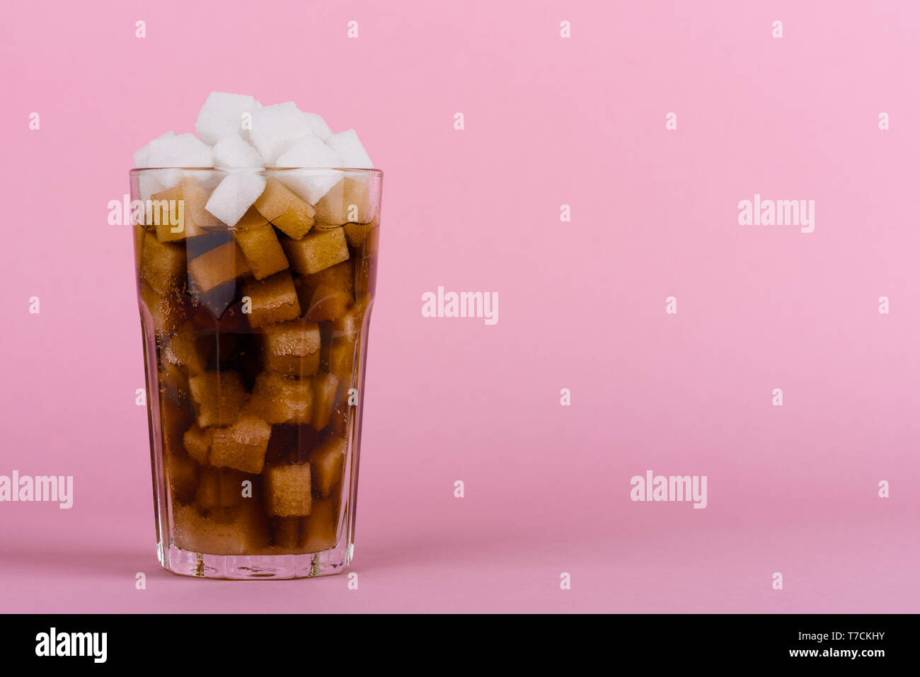 Verre à boire de cubes de sucre en morceaux et douce boisson coca sur rose pastel arrière-plan. Unhealthly régime avec des boissons gazeuses sucrées doux concept. Banque D'Images